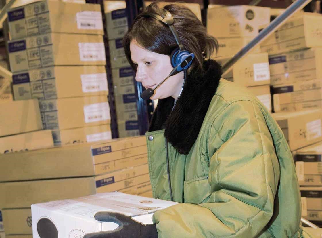 La préparatrice de commandes réalise son travail avec un système de voice picking. La préparatrice de commandes réalise son travail avec un système de voice picking.